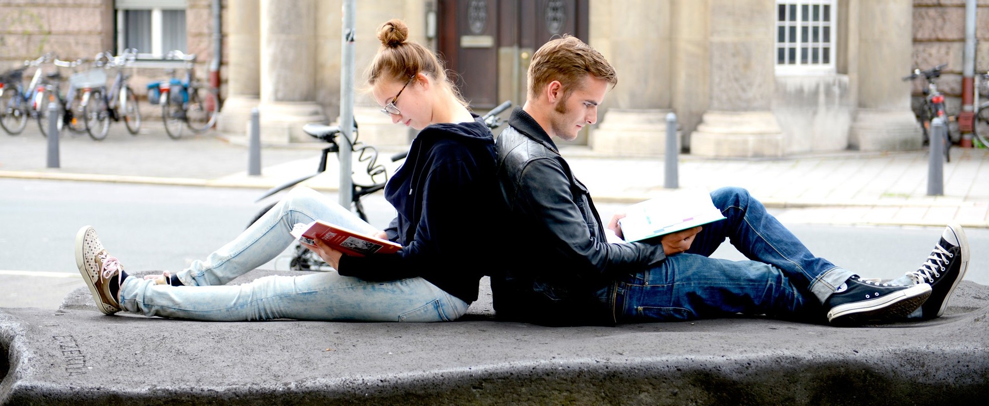 Zwei junge Leute sitzen Rücken an Rücken und lesen