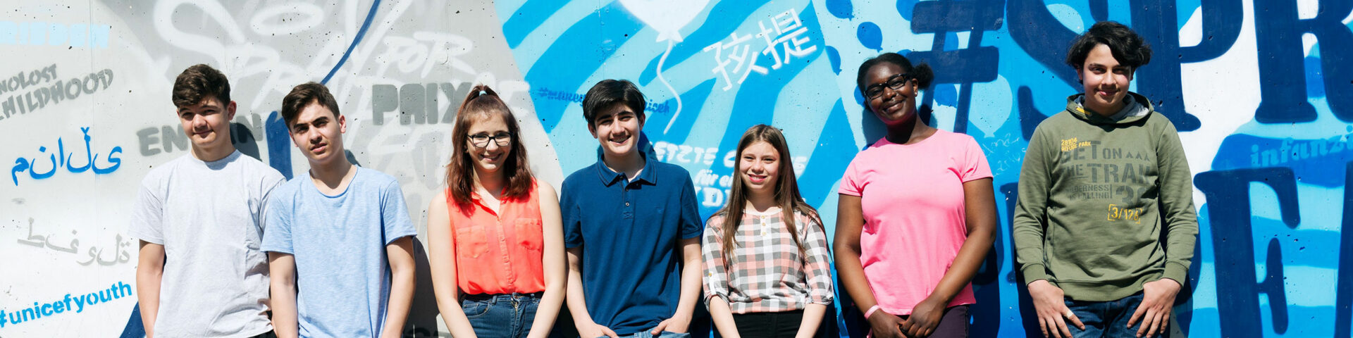 Eine Gruppe junger Menschen steht vor einer blau bemalten Wand.