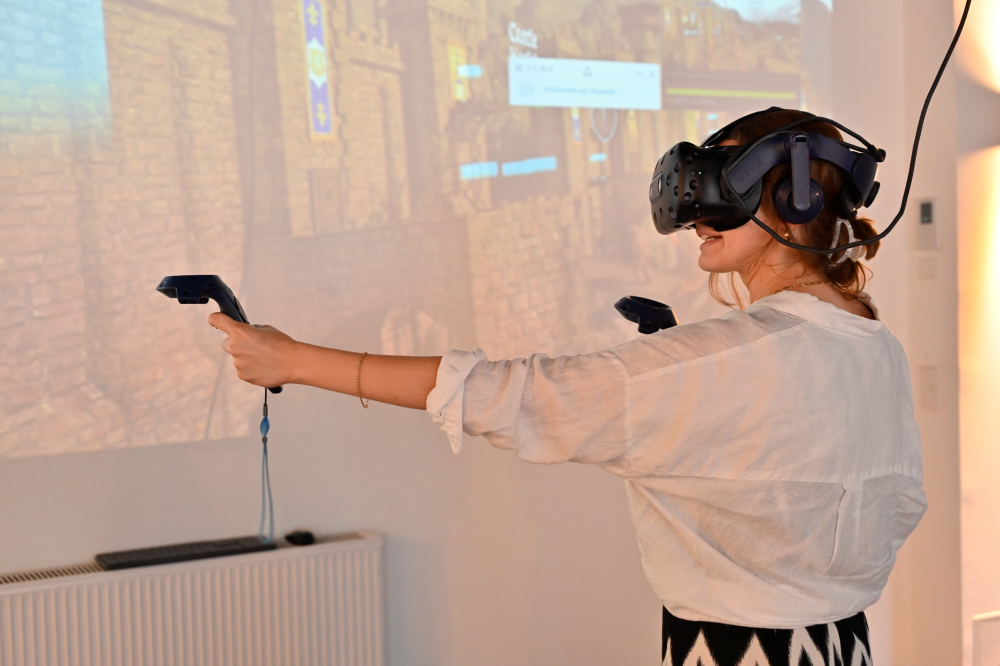 Eine Frau trägt eine VR-Brille und hat zwei Controller in den Händen.