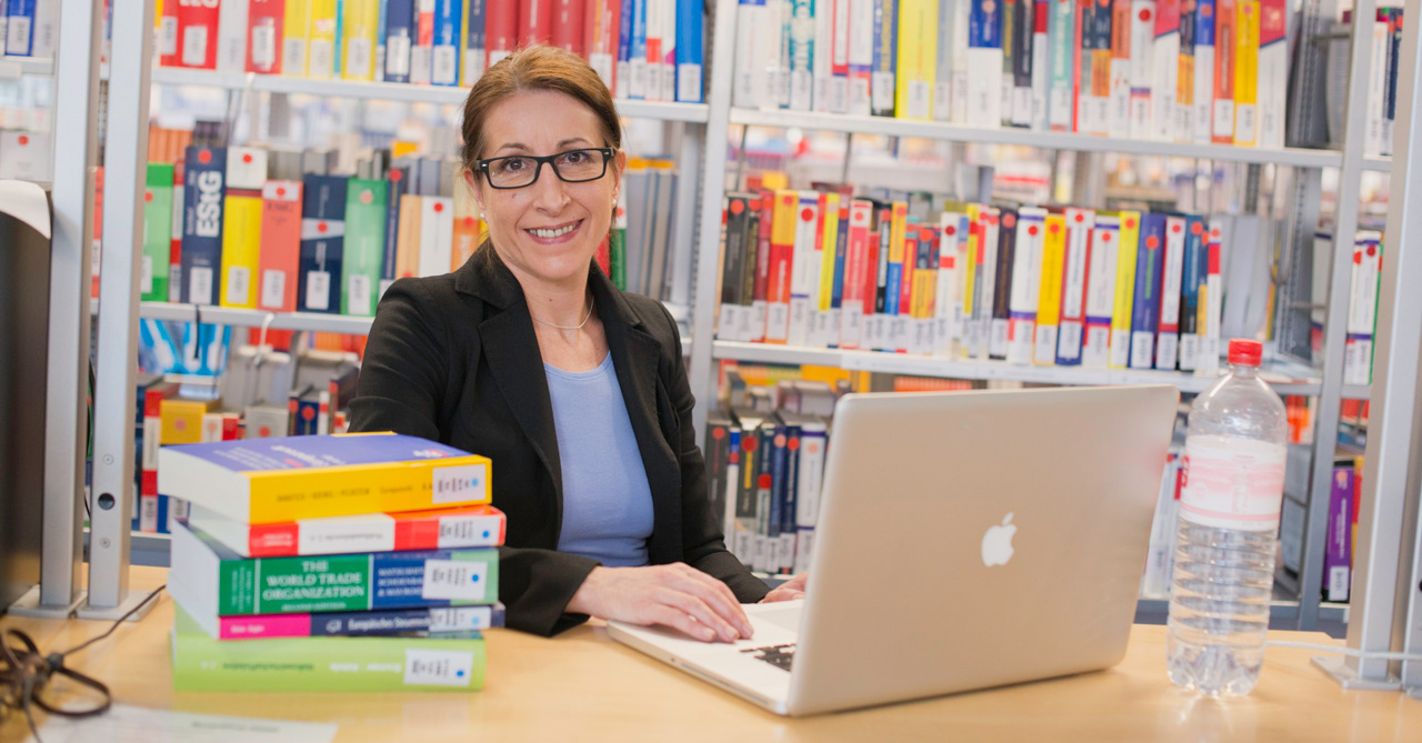Eine Frau sitzt mit einem Laptop in einer Bibliothek.