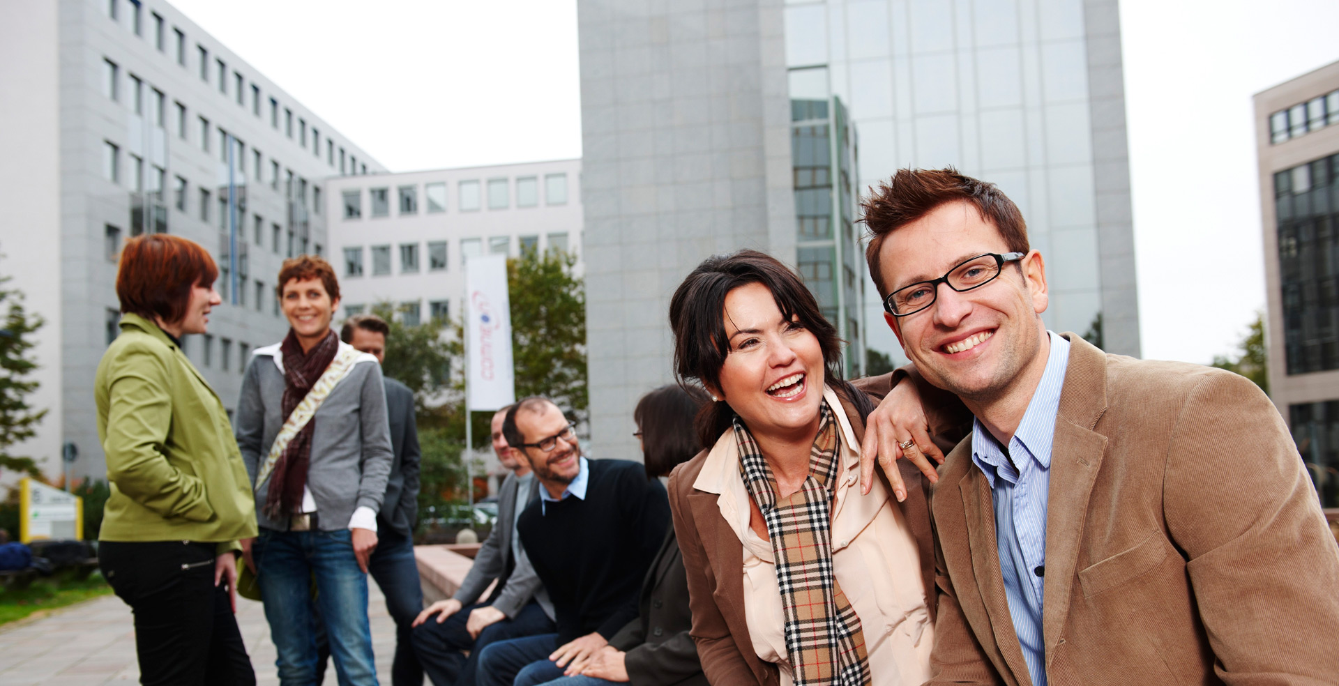 Eine Gruppe Erwachsene sitzen vor Bürogebäuden und unterhalten sich.
